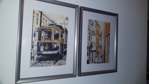 Two framed artworks depicting vintage tram cars in an urban setting. - Apartment Suite - Rio Douro Ribeira Historic Center  (Porto)