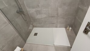 A shower area with a glass door, a white shower seat, and a small shelf with toiletries. - Apartment Suite - Rio Douro Ribeira Historic Center  (Porto)