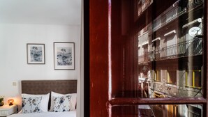 A hotel room with a bed, two framed floral artworks on the wall, and a view of the street through a wooden door. - Apartment Suite - Rio Douro Ribeira Historic Center  (Porto)
