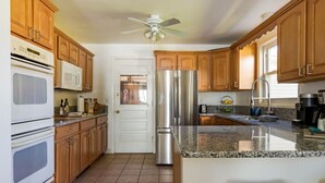 A kitchen with wooden cabinets, stainless steel appliances, a granite countertop, and a ceiling fan.