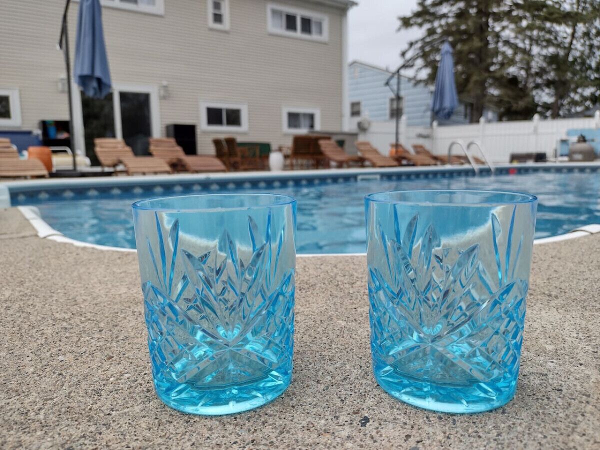 Två genomskinliga glasglas med en blåaktig nyans, placerade på en betongyta nära en swimmingpool.