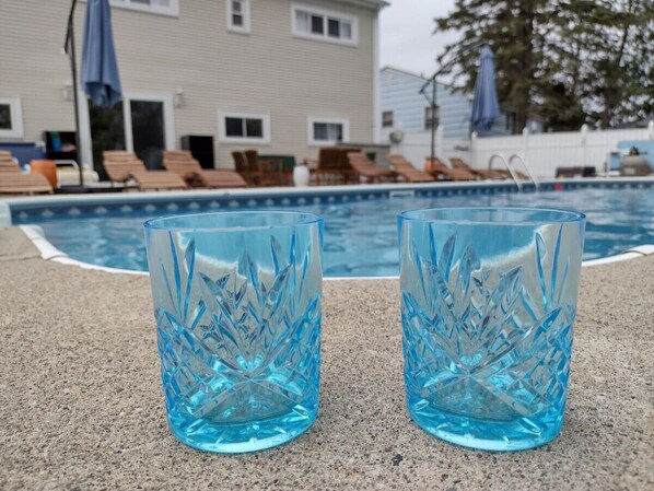 Dos vasos de vidrio transparentes con un ligero tono azul sobre una superficie de concreto cerca de una piscina.