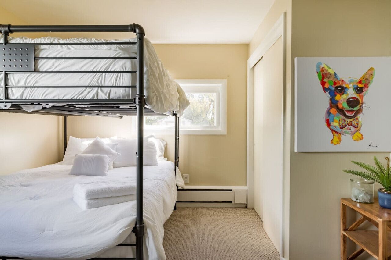 A bunk bed room with a window, a painting of a dog, and a small plant on a side table.