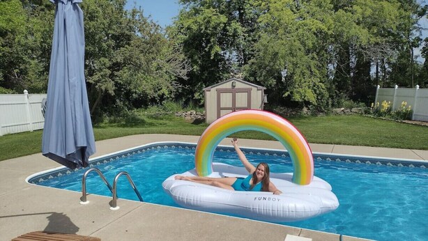 A swimming pool with a rainbow inflatable float, lounge chairs, and a small shed in the background.