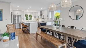 A modern kitchen with white cabinets, stainless steel appliances, and a wooden dining table with benches. - OCEAN VIEWS | 2nd Row | Heart of EI | NEWLY RENOVATED!! (Emerald Isle)