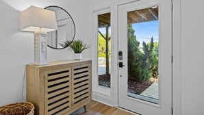 A white door with a glass panel, a wooden console table with a lamp, and a potted plant. - OCEAN VIEWS | 2nd Row | Heart of EI | NEWLY RENOVATED!! (Emerald Isle)