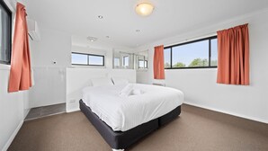 Een moderne slaapkamer met een groot bed, witte muren en uitzicht op bomen door het raam.