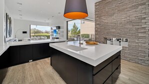 A modern kitchen with a large island, dark cabinetry, and a stone accent wall.