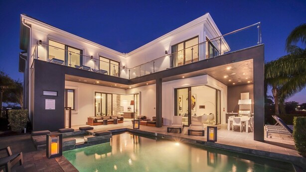 A modern two-story house with a swimming pool, outdoor seating, and a balcony.