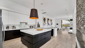 A modern kitchen with a central island, white cabinetry, and a hanging pendant light.