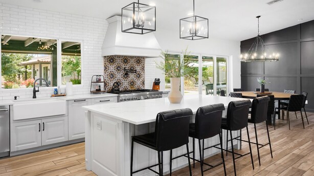 Een moderne keuken met witte kasten, een groot eiland met barstoelen en hanglampen.