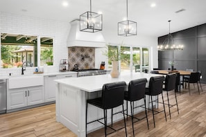 A modern kitchen with white cabinetry, a large island with bar stools, and pendant lighting.