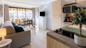 Un soggiorno moderno con un divano, un tavolino in vetro e una zona pranzo con tavolo e sedie. È presente anche un angolo cottura con un forno a microonde e una pianta.