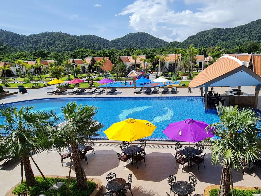 A resort pool area with lounge chairs, umbrellas, and a view of a mountainous landscape.