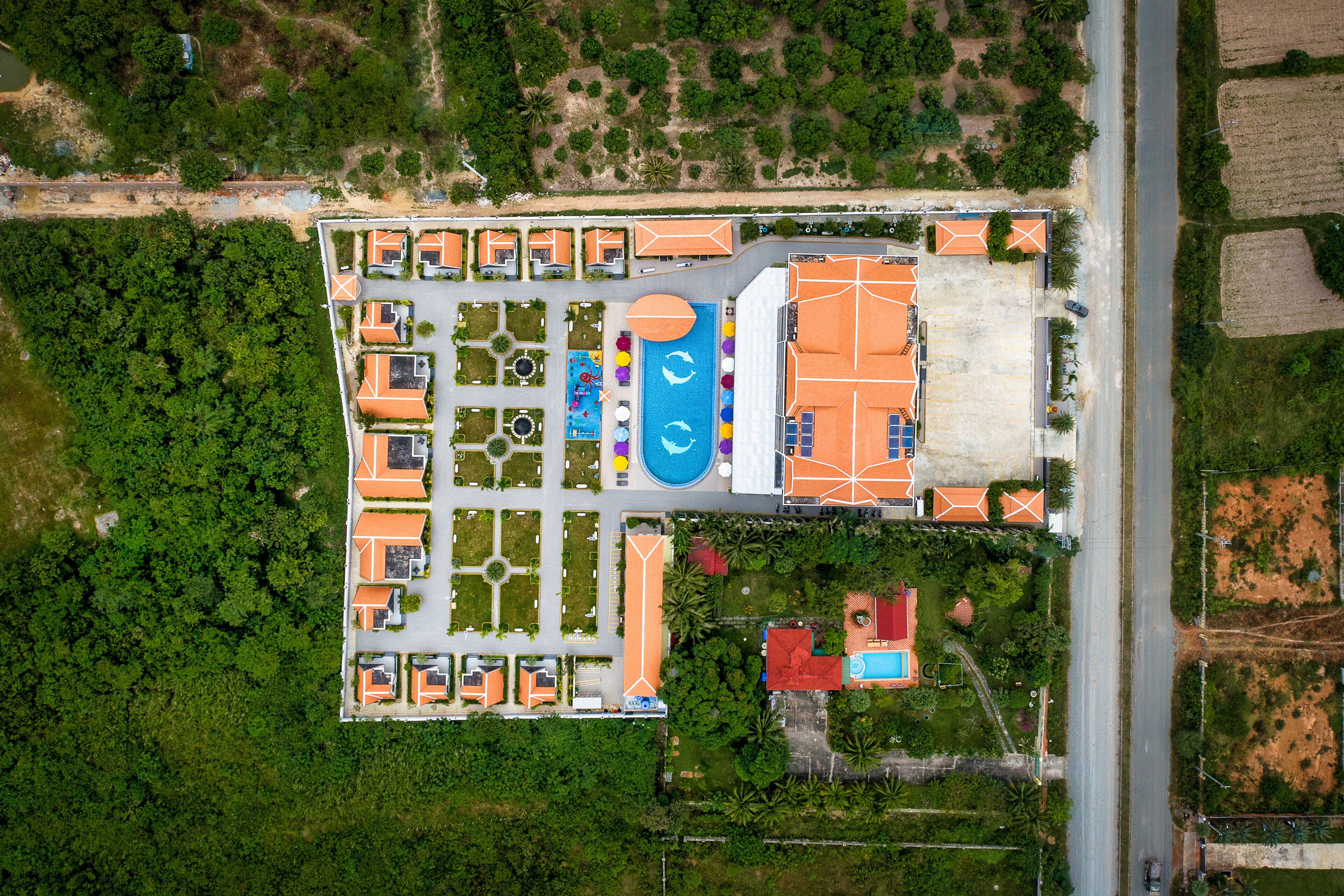 Vue aérienne d’un complexe hôtelier comprenant plusieurs bâtiments, une piscine et une végétation luxuriante.