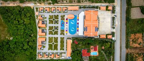 Vue aérienne d’un complexe hôtelier comprenant plusieurs bâtiments, une piscine et une végétation luxuriante.