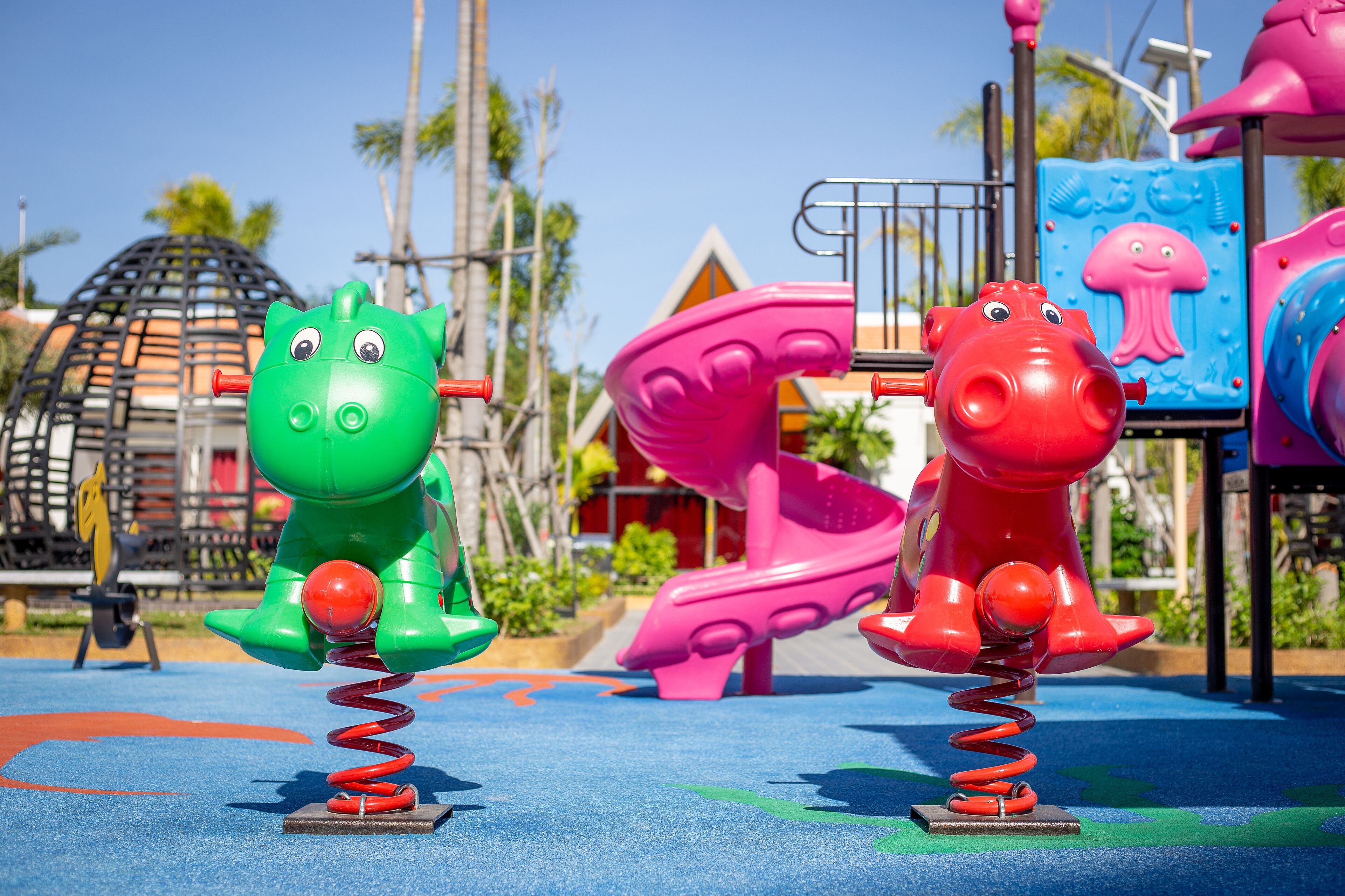 A playground with two swings, one green and one red, and a slide in the background.