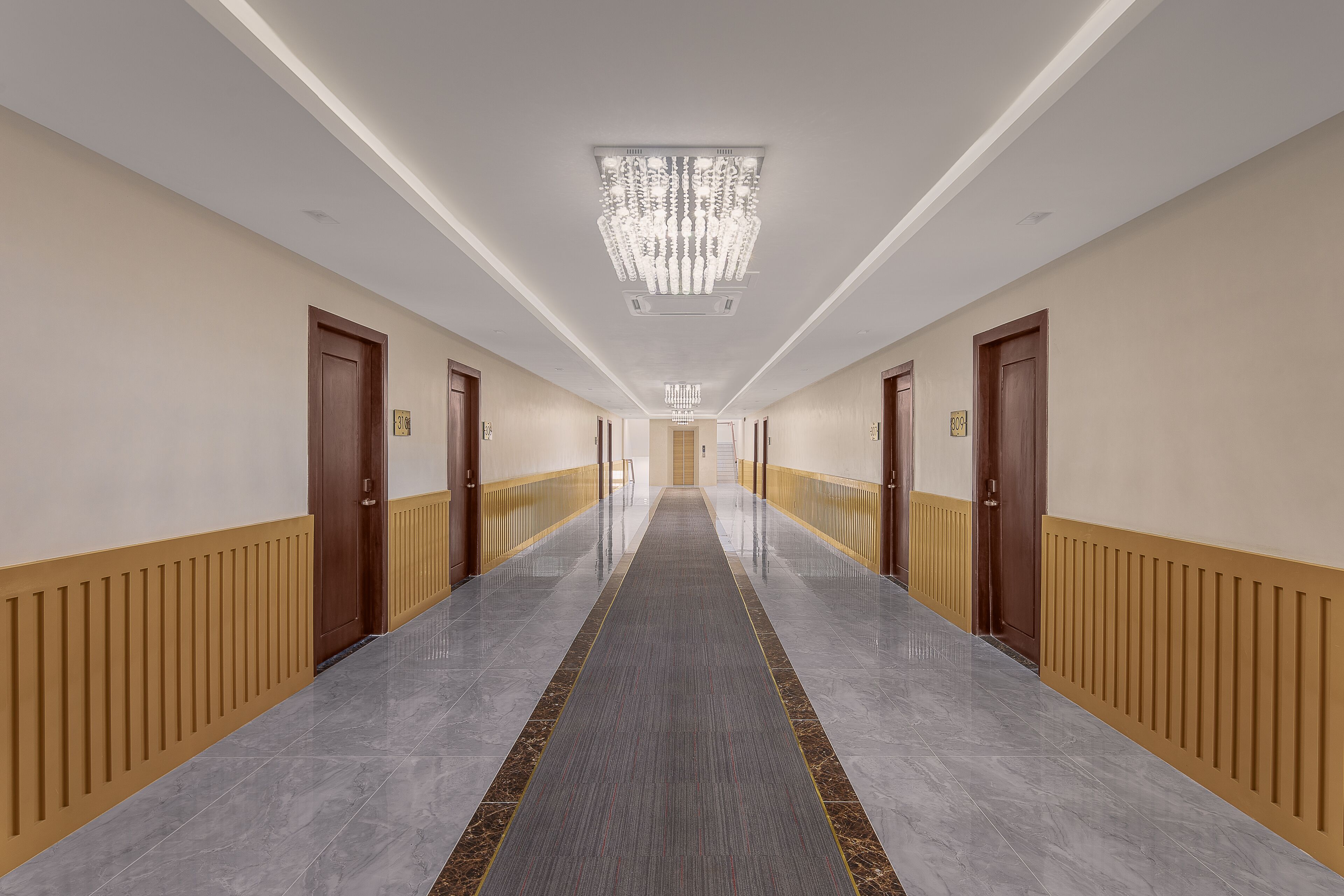 A long, well-lit hallway with a central carpeted path, flanked by wooden doors and beige walls.