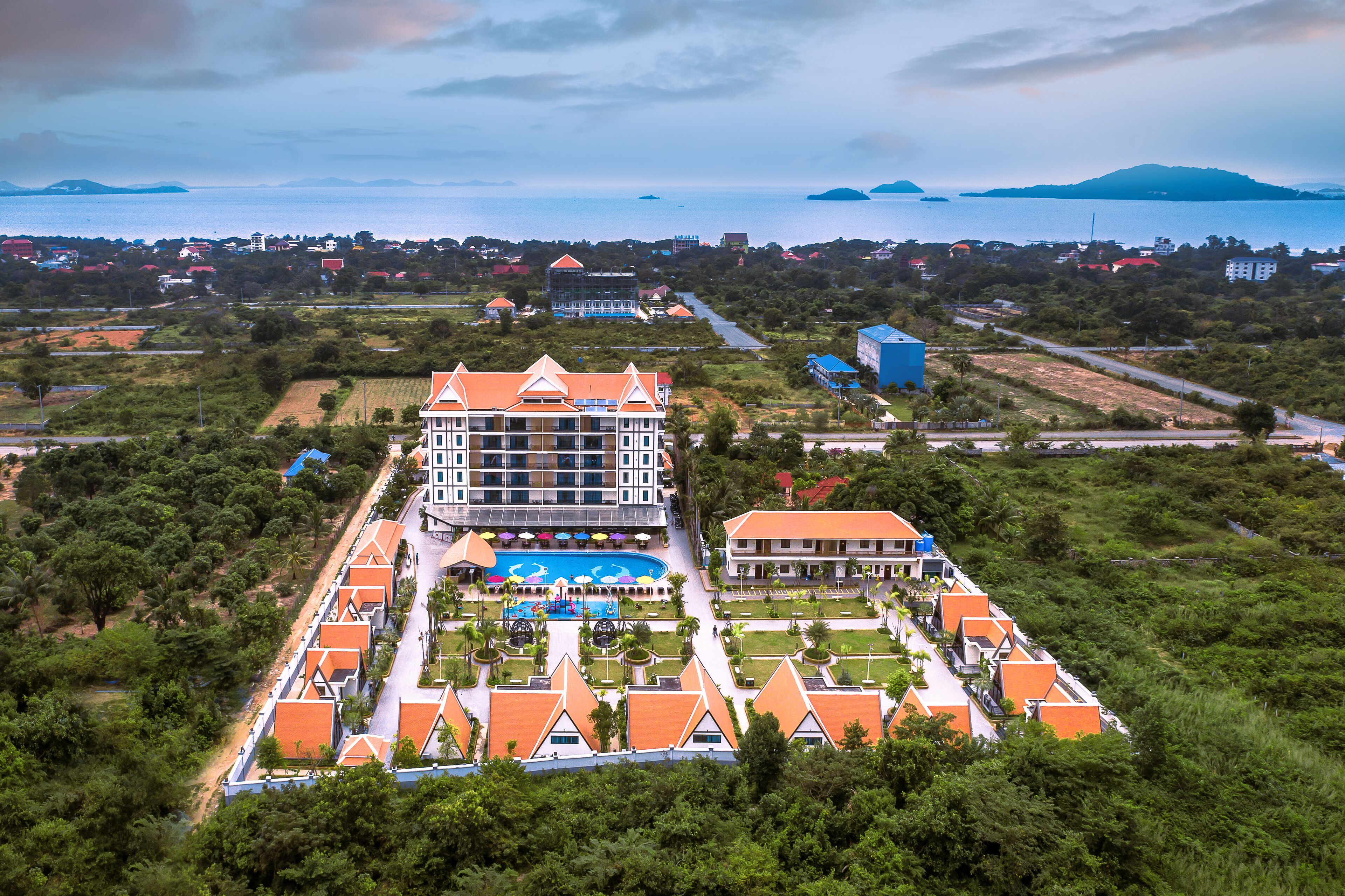 An aerial view of a resort with multiple buildings, a swimming pool, and a view of the sea.