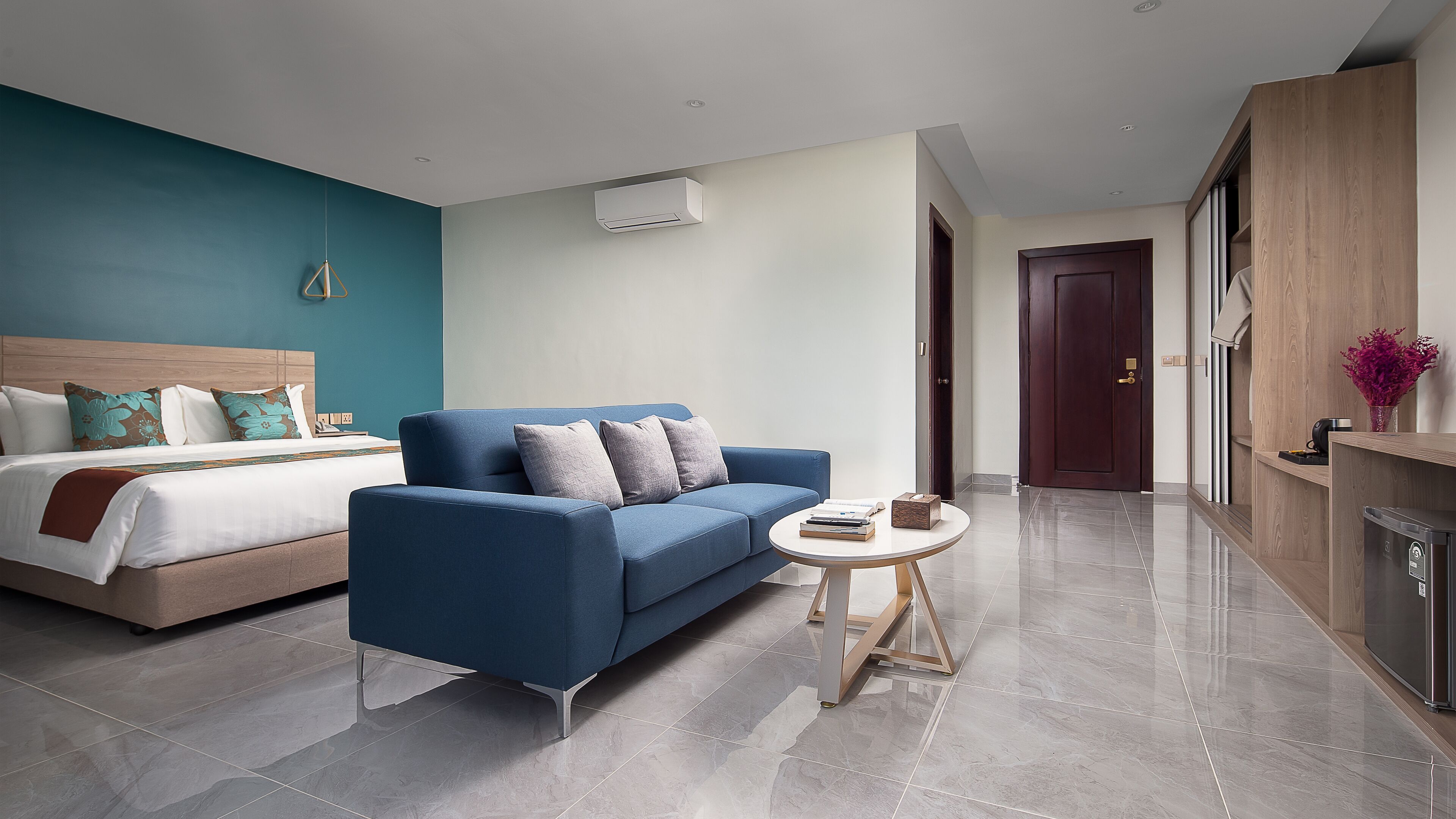 A modern hotel room with a bed, a blue sofa, a small round table, and a wardrobe.