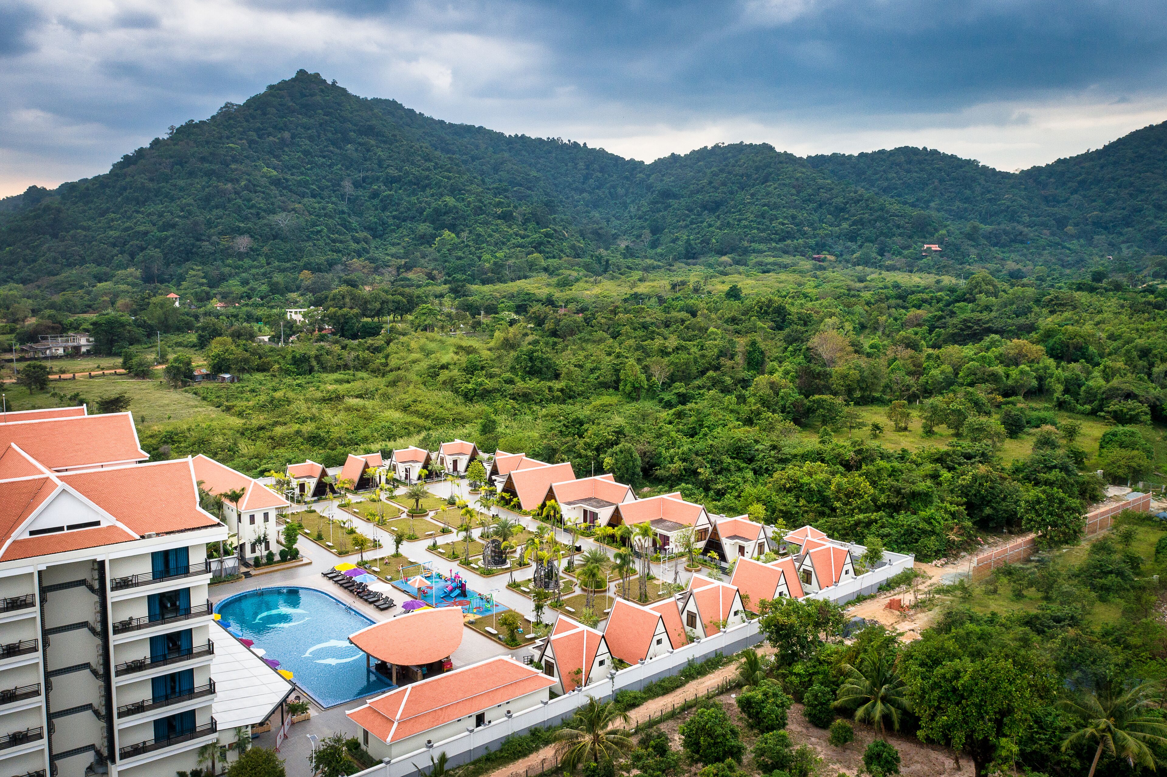 A resort with multiple bungalow-style buildings, a swimming pool, and lush greenery surrounding the property.