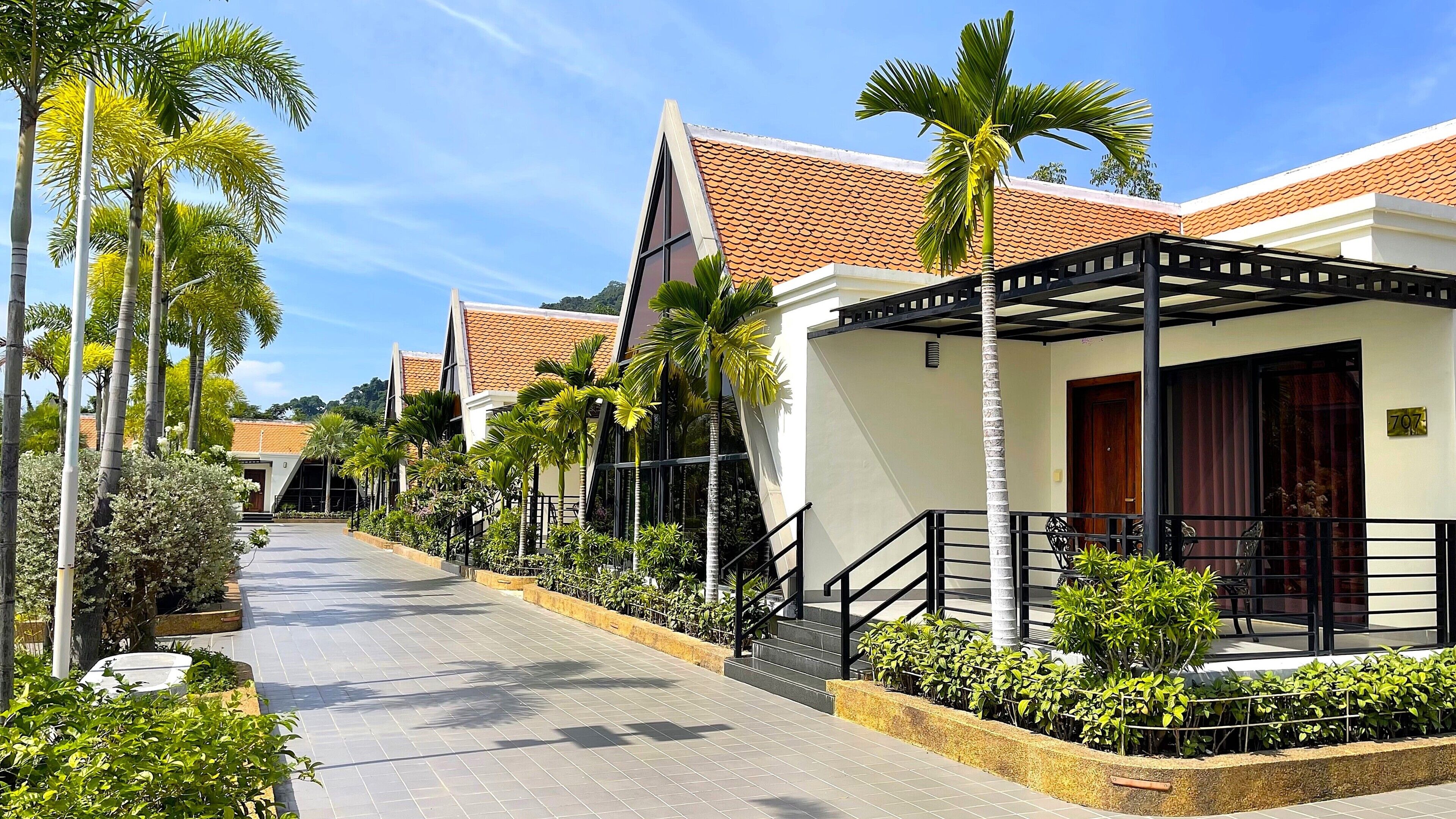 A hotel corridor with a covered walkway, palm trees, and a tiled roof.