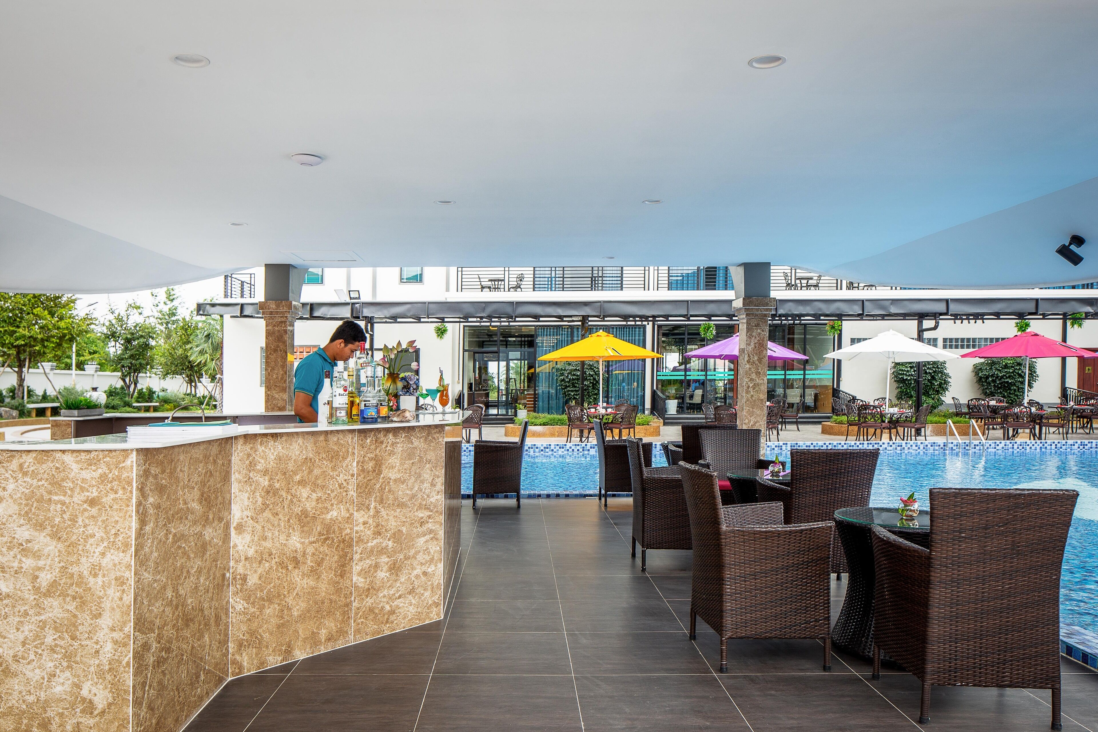 Zona junto a la piscina con bar, muebles de mimbre y sombrillas.