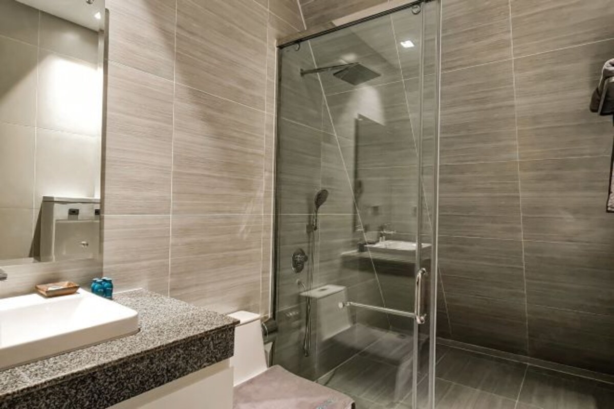 A modern bathroom with a glass-enclosed shower, a granite countertop, and a large mirror.