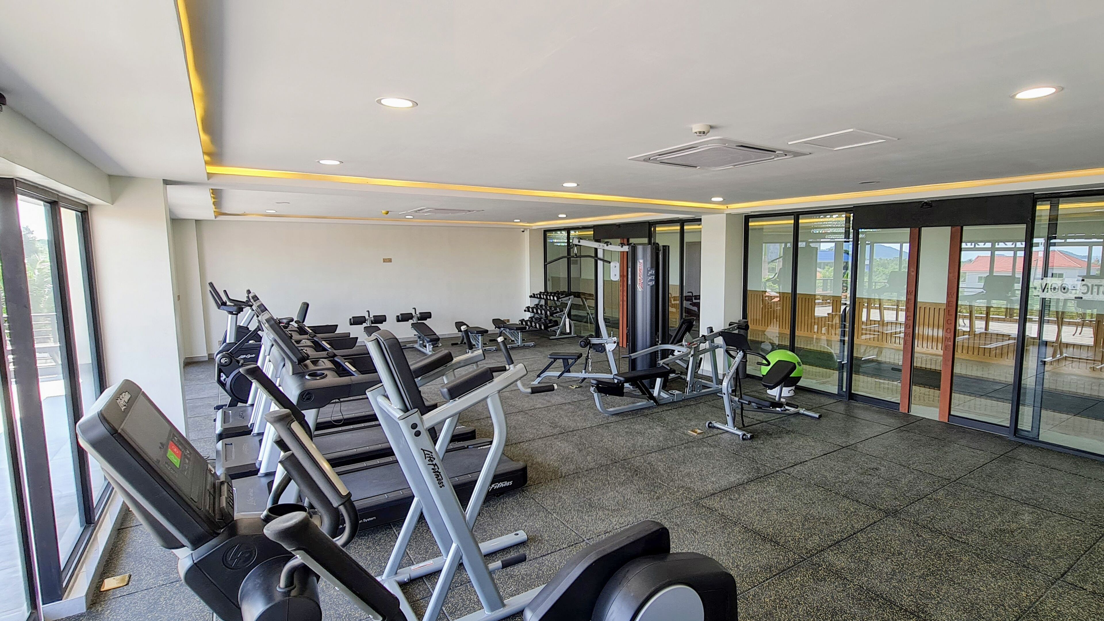 Uma academia com esteiras, aparelhos de musculação e um espelho grande.