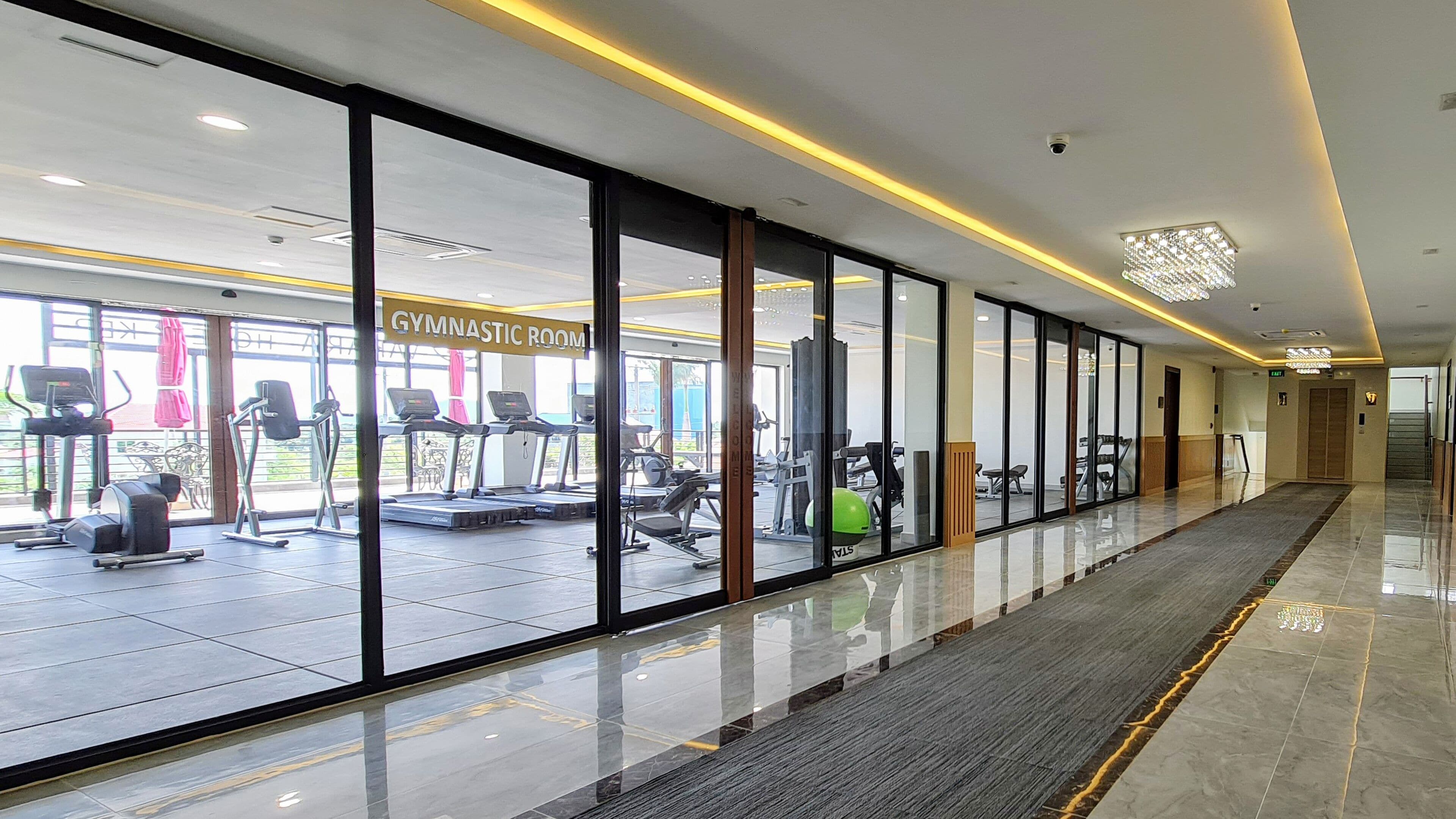 A gym with exercise equipment, a sign reading "GYMNASTIC ROOM", and a polished floor.