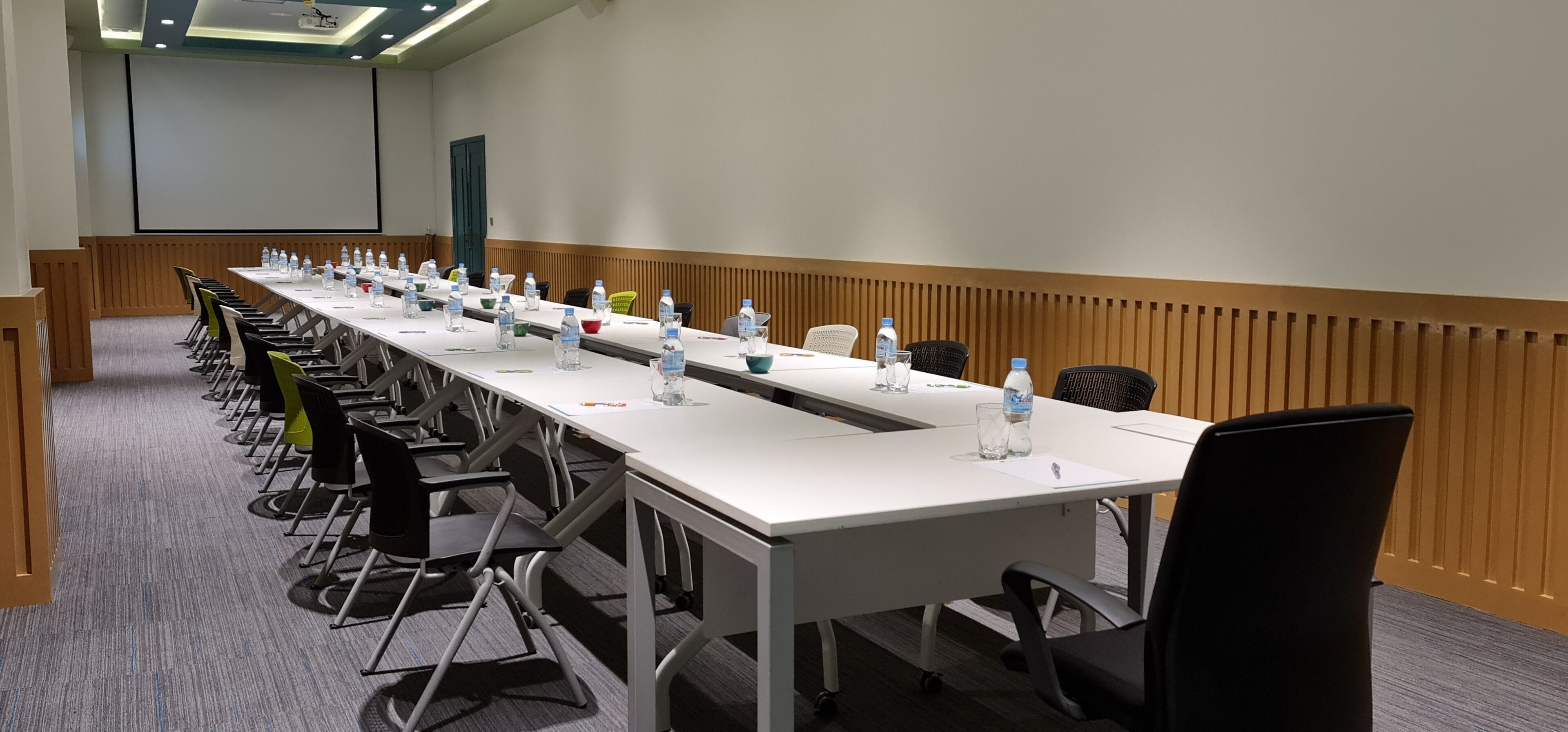A conference room with a long table, chairs, water bottles, and a projector screen.