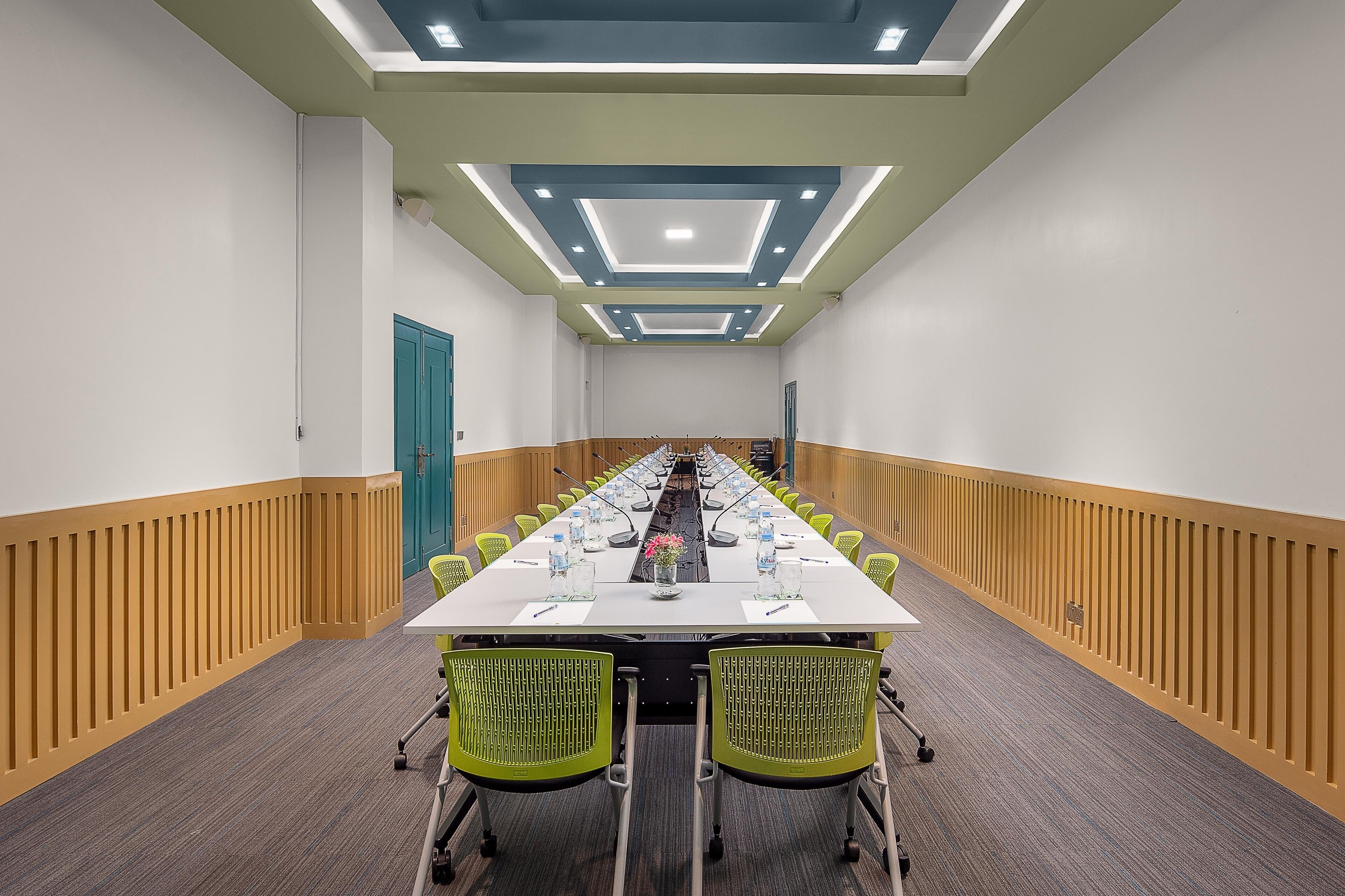 Ett konferensrum med ett långt bord, gröna stolar och väggar som har en träpaneldesign.