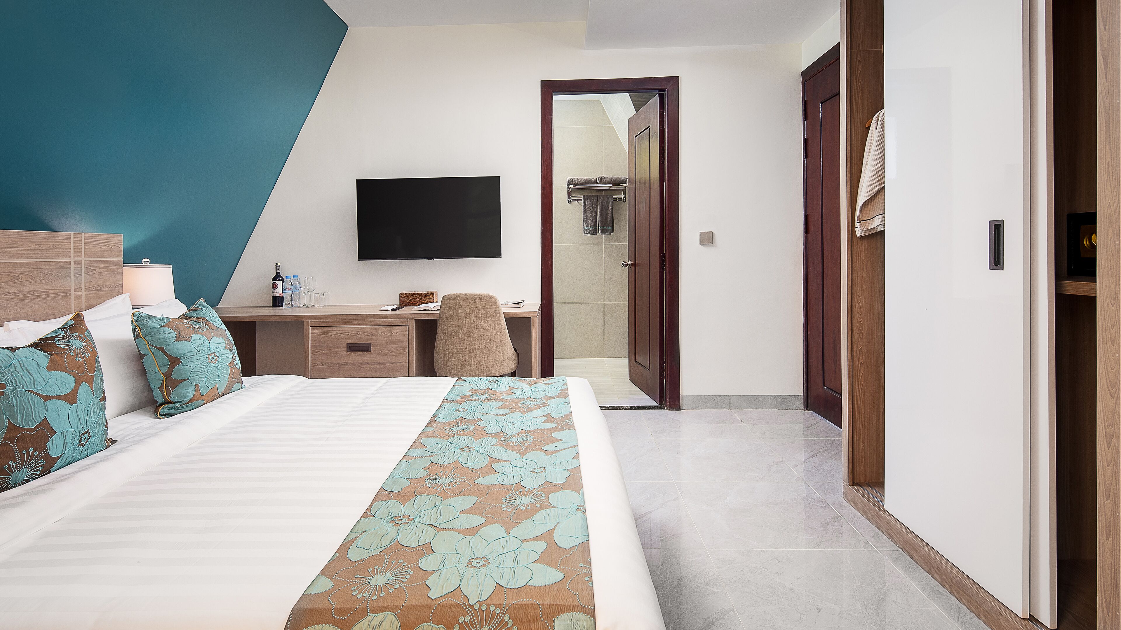 Una habitación de hotel moderna con cama, escritorio, silla, televisor de pantalla plana y un baño visible a través de una puerta abierta.