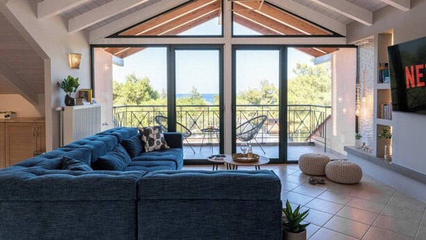 A modern living room with a large sectional sofa, a balcony with outdoor furniture, and a large window offering a view of the outdoors. - Gregory's loft (100 meters from the beach) (Αγία Άννα, Εύβοια)