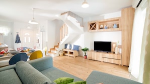 Un salon moderne avec un escalier, un téléviseur à écran plat et un coin repas comprenant des chaises et une table.