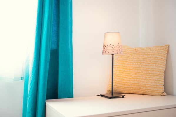 A bedside table with a lamp and a patterned pillow against a white wall.