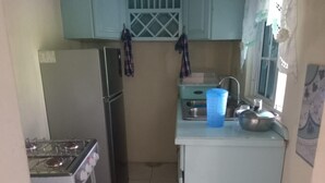 A compact kitchen with a gas stove, refrigerator, and a small countertop with a sink and a blue container.