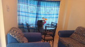 A living room with a blue sofa, patterned cushions, a small table, and chairs.