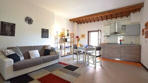A living room with a sofa, a dining table with chairs, a kitchen area with cabinets and a sink, and a clock on the wall. - 2 Bed-Sleeps 6-AirCon-Town Centre-Free Parking (Montagnana)