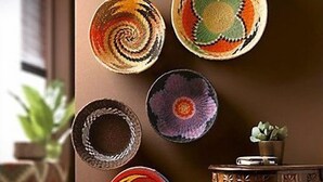 A room with a brown wall adorned with six colorful woven bowls. A small wooden table with a plant and a stack of books is in the foreground. - The Studio | Nairobi | 5* Luxury (UN & Two Rivers) (Ruaka, Nairobi)