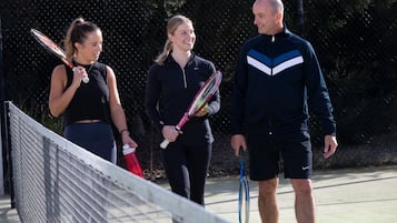 Un court de tennis avec un filet, une clôture et une personne tenant une raquette de tennis.