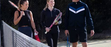 Een tennisbaan met een net, een hek en een persoon die een tennisracket vasthoudt.