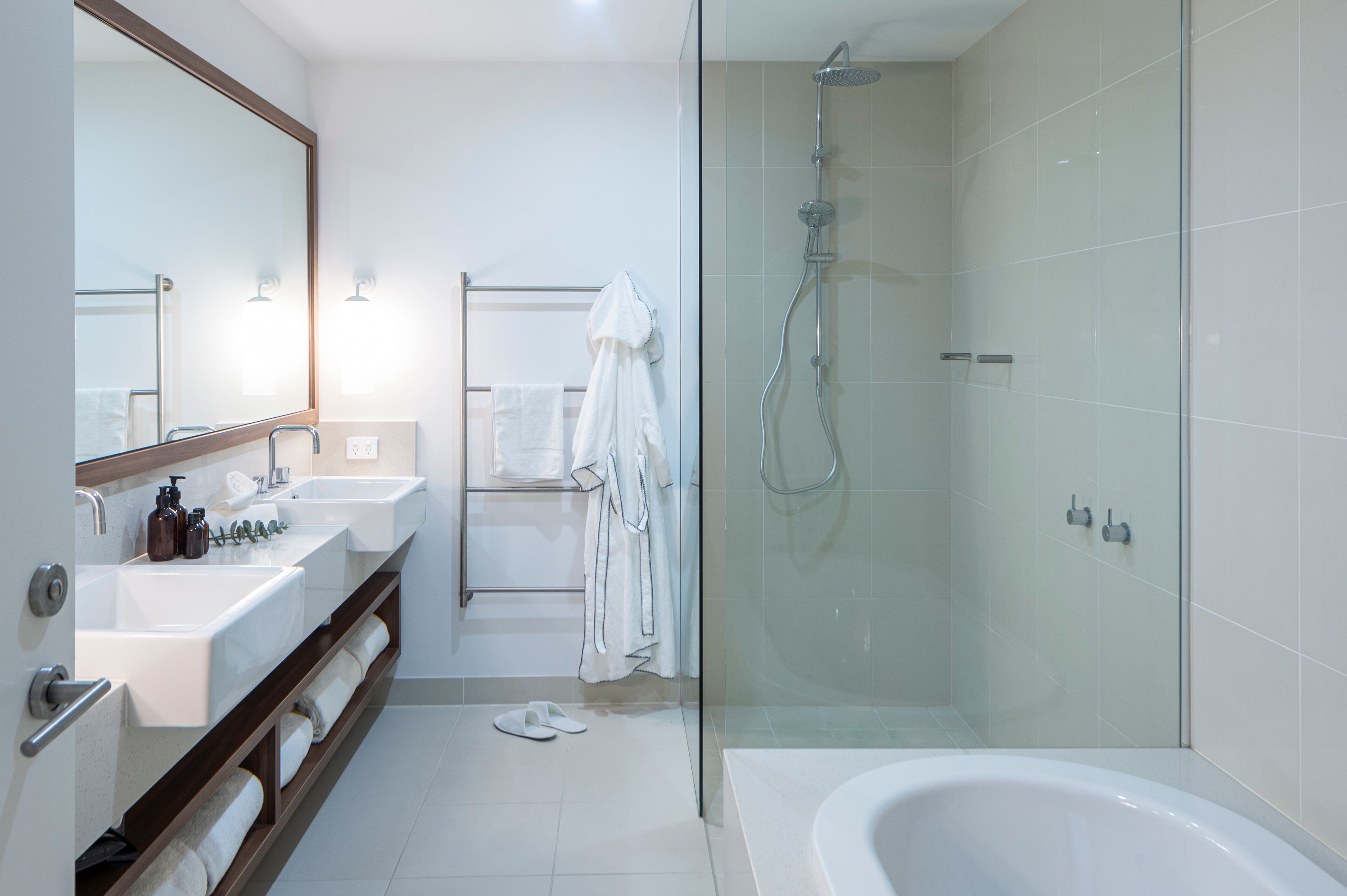 A modern bathroom with a glass-enclosed shower, a large bathtub, and a vanity with two sinks.
