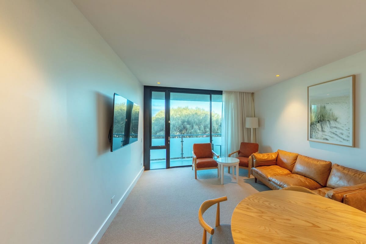 Ein modernes Hotelzimmer mit großem Fenster, einer Couch, einem Tisch und einem an der Wand befestigten Fernseher.