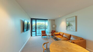 Una habitación de hotel moderna con un ventanal grande, un sofá, una mesa y un televisor montado en la pared.