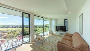 A spacious living room with a large TV, comfortable seating, and a balcony with a view of the countryside. - The Sands Torquay (Torquay)