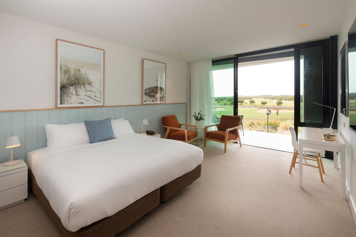 Ein Hotelzimmer mit einem großen Bett, zwei Stühlen, einem Schreibtisch und Blick auf einen Golfplatz.