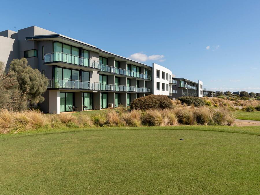A modern building with multiple balconies, large windows, and a well-maintained lawn.