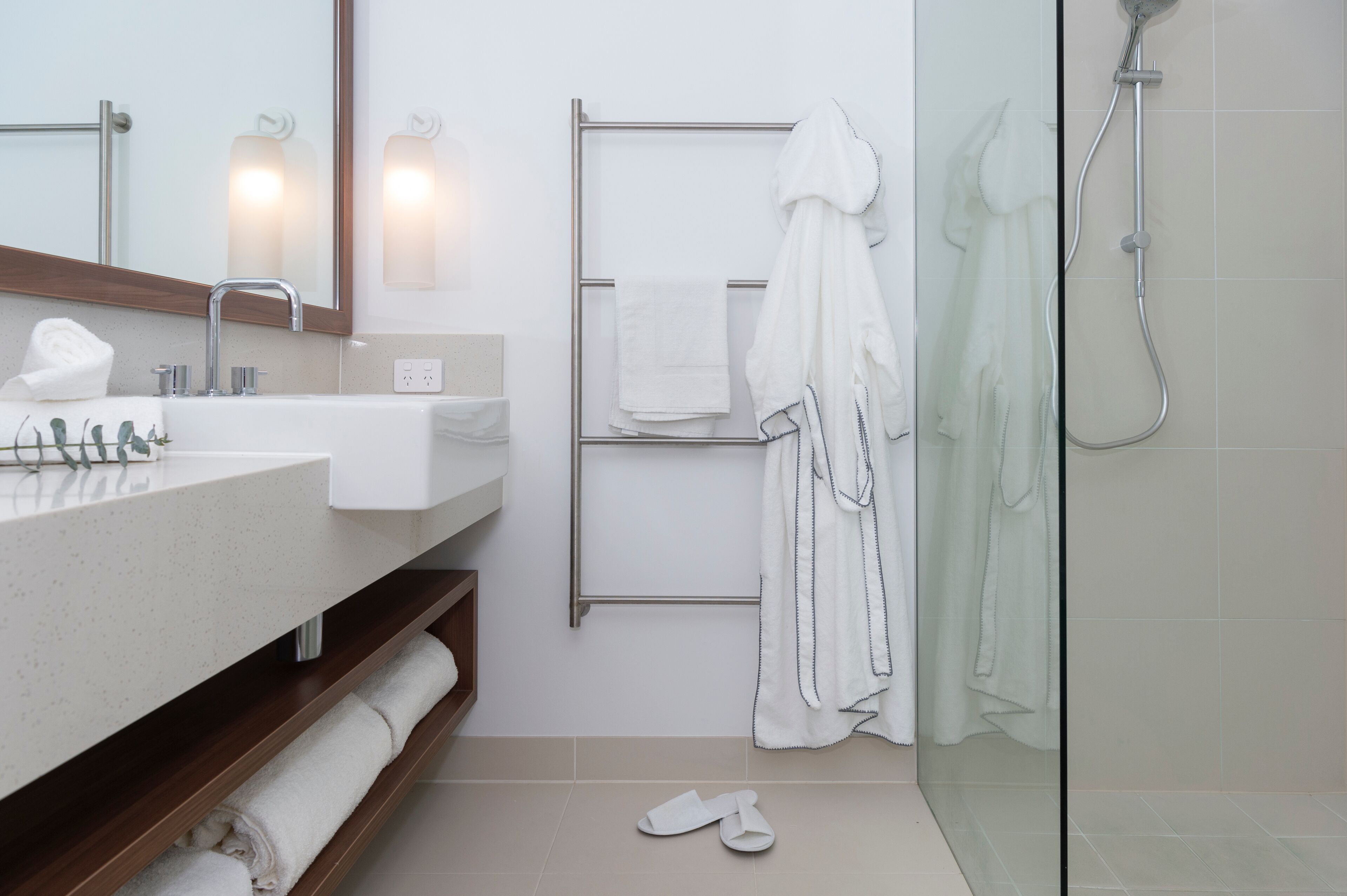 A modern bathroom with a glass-enclosed shower, a sink with a mirror, and a towel rack with multiple towels.