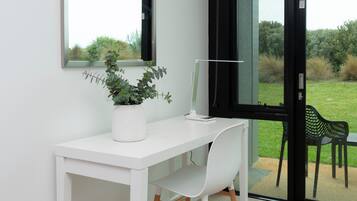 A white desk with a potted plant, a computer, and a chair in front of a window with a view of greenery.